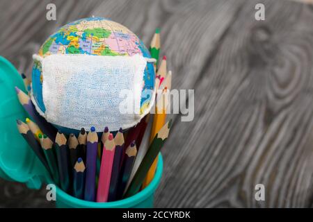 Matite colorate in un porta matita. Nelle vicinanze si trova un globo con una maschera medica. Anno accademico durante l'epidemia. Foto Stock