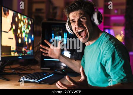 Immagine di un giovane furioso in cuffia che urla durante il gioco videogioco sul computer a casa Foto Stock