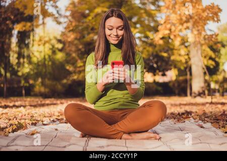 Foto di carino affascinante signora autunno parco foglie coperto terreno siediti coperta a piedi nudi tenere telefono chattando amico all'estero rapporto bello usura da agenti atmosferici Foto Stock