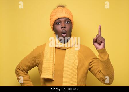 L'uomo africano soddisfatto in vestiti di inverno che mostra le dita di indice in su, dando consiglio Foto Stock