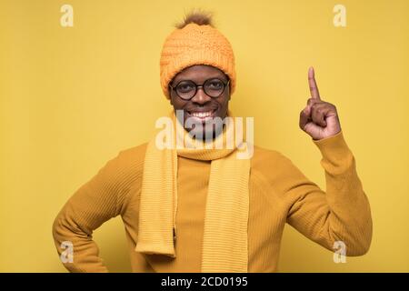 L'uomo africano soddisfatto in vestiti di inverno che mostra le dita di indice in su, dando consiglio Foto Stock