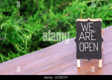 Testo scritto a mano Siamo aperti su lavagna closeup su caffè tavola di legno all'aperto. Accesso aperto al caffè all'aperto che invita i clienti. Aprire il segno come simbolo o Foto Stock