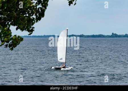 Un uomo sta navigando su un catamarano al contrario riva del lago Foto Stock