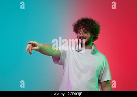 Puntamento, visualizzazione. Ritratto di un giovane caucasico su sfondo studio gradient in luce al neon. Bella modello maschile in stile casual. Concetto di emozioni umane, espressione facciale, gioventù, vendite, pubblicità. Foto Stock