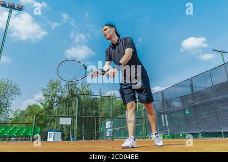 Il giocatore di Tennis piano lontano dell'uomo si prepara a servire una palla da tennis alla partita. Foto Stock