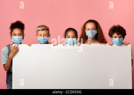 Gruppo di bambini in maschere protettive con banner vuoto spazio per il design su sfondo rosa Foto Stock