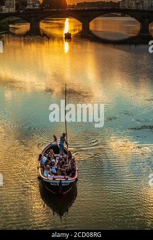 una piccola barca piena di turisti (il cosiddetto renaiolo) Galleggia sul fiume Arno di Firenze al tramonto Foto Stock