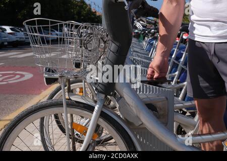 Un giovane uomo sportivo irriconoscibile che noleggia una bicicletta dallo stand di condivisione in una città. Valencia, Spagna. Foto Stock