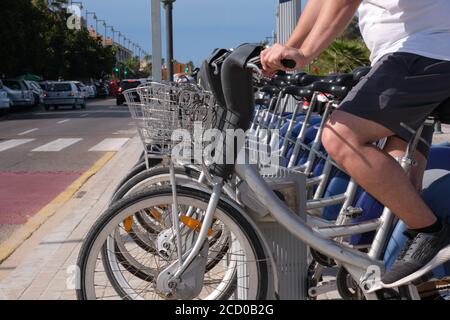 Un giovane uomo sportivo irriconoscibile che noleggia una bicicletta dallo stand di condivisione in una città. Valencia, Spagna. Foto Stock