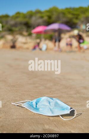 primo piano di una maschera chirurgica blu usata gettata sulla sabbia bagnata della riva di una spiaggia Foto Stock