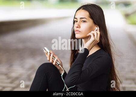 Giovane donna che ascolta la musica mentre si siede sul lungomare Foto Stock