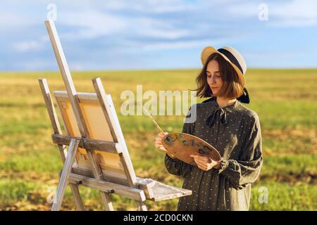 Giovane artista donna dipinge un quadro all'aperto su un caldo estate sera Foto Stock