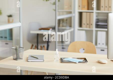 Immagine di sfondo della scrivania vuota del luogo di lavoro con maschera facciale e disinfettante per le mani nell'ufficio post pandemico, spazio di copia Foto Stock