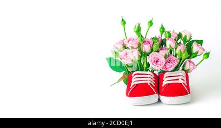 Paio di scarpe rosse per bambini piene di fiori di rose su sfondo bianco. Spazio vuoto per il testo. Foto Stock