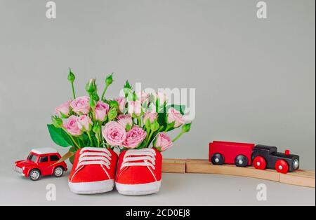 Paio di scarpe rosse per bambini piene di fiori di rose su sfondo grigio. Spazio vuoto per il testo. Foto Stock
