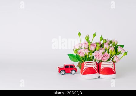 Paio di scarpe rosse per bambini piene di fiori di rosa e giocattolo per auto su sfondo chiaro. Spazio vuoto per il testo. Foto Stock