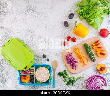 Concetto di cibo sano. Scatola per pranzo blu con coperchio riempito con sandwich, croccanti, frutta e verdura e ingredienti su sfondo chiaro con blan Foto Stock