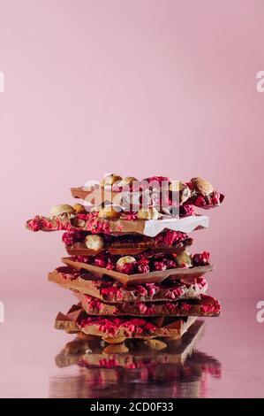 Barrette di cioccolato spezzate fatte a mano decorate con nocciole intere, mandorla e lampone sublimato su sfondo rosa con spazio vuoto per il testo; selettivo Foto Stock