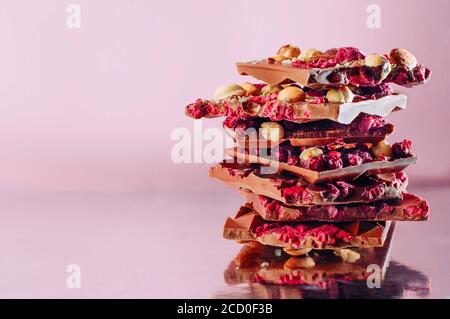 Barrette di cioccolato spezzate fatte a mano con surafce decorate con nocciole intere, mandorla e lampone sublimato su sfondo rosa con spazio copia; selezionare Foto Stock