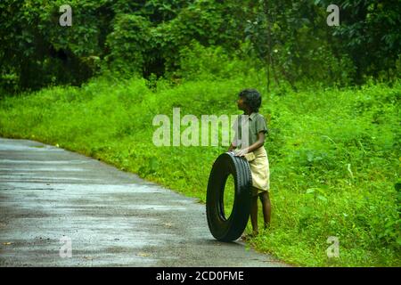 Ragazzo tribale che gioca con un pneumatico di automobile, terra propria del dio, attrazione turistica del Kerala di sfondo verde bello, cultura popolare del villaggio del Kerala Foto Stock