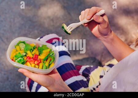 Concetto di cibo sano: Primo piano di una giovane donna che mangia dal pranzo al sacco riempito con insalata all'aperto. Messa a fuoco selettiva, vista dall'alto Foto Stock