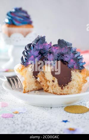 Cupcake alla vaniglia con panna montata scura galassia e ripieno di cioccolato tagliare a metà su sfondo chiaro Foto Stock