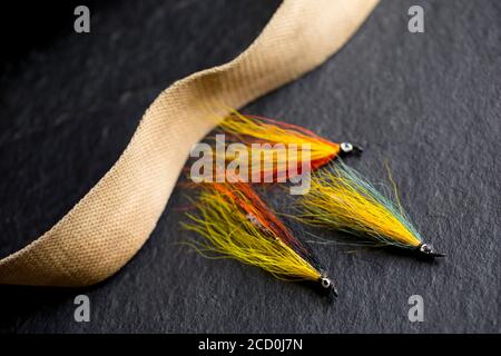 Tre mosche di salmone che erano probabilmente fatte in casa su uno sfondo di ardesia scuro accanto alla cinghia da una vecchia scatola di attacco di vimini. Dorset Inghilterra Regno Unito GB Foto Stock