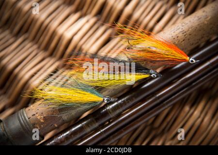 Tre mosche di salmone che erano probabilmente fatte in casa sul manico di sughero di una vecchia canna da pesca della mosca che riposa su una scatola di attacco di vimini. Da una collezione di tinta Foto Stock