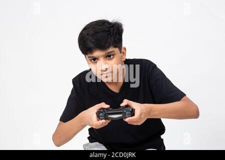 Giovane ragazzo indiano che tiene la console di gioco in mano. Carino adolescente che gioca a videogiochi con il suo controller Foto Stock