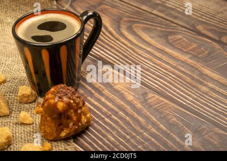Una tazza di caffè, pezzi di zucchero di canna e una torta sul tavolo di legno. Primo piano Foto Stock