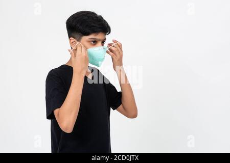 Il giovane ragazzo indiano indossa una maschera facciale per la protezione contro Covid-19. Cute teenager mette sulla maschera Foto Stock