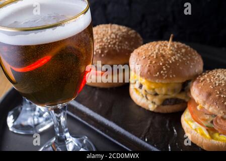 primo piano, bicchieri da birra con birra artigianale scura e chiara con schiuma, sullo sfondo di hamburger, con una varietà di ingredienti, tra cui lo shyomga Foto Stock