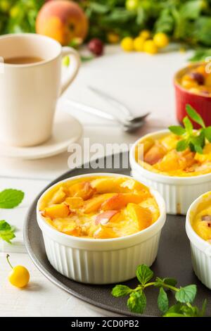 Deliziosa clafoutis a base di yogurt bianco e pesche, ciliegia e dessert di pesca in ciotole porzionate sul tavolo con una tazza di succo Foto Stock