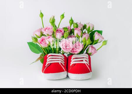 Paio di scarpe rosse per bambini piene di fiori di rosa su sfondo bianco. Spazio vuoto per il testo. Foto Stock