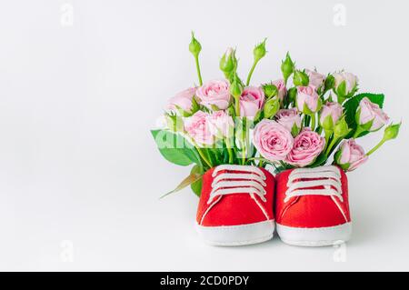 Paio di scarpe rosse per bambini piene di fiori di rosa su sfondo chiaro. Spazio vuoto per il testo. Foto Stock