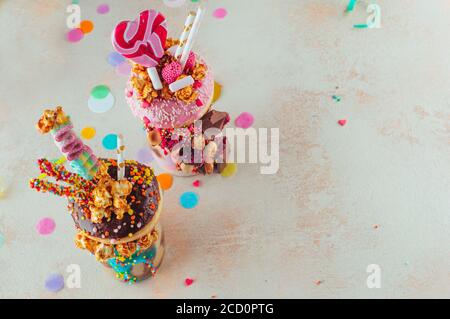 Concetto di festa dei bambini: Vista dall'alto di due frullati di freak con ciambelle, popcorn al caramello e dolci sullo sfondo della festa con spazio vuoto per il testo Foto Stock
