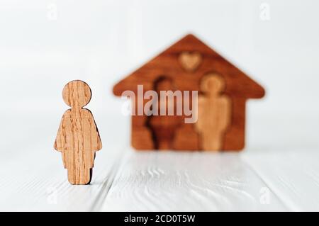 Figura femminile di legno di fronte alla casa su sfondo bianco come simbolo di problemi nei rapporti familiari. Focus sulla figura femminile, spazio vuoto per il testo Foto Stock