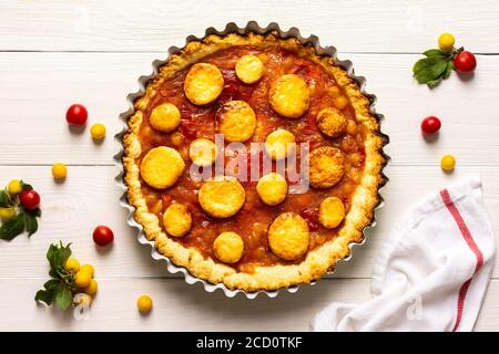 Torta aperta di pasta frolla con prugna di ciliegia, clafoutis di prugna mirobalana su sfondo bianco Foto Stock