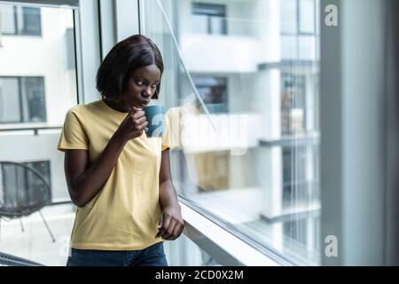 African American donna nel suo soggiorno a bere tenendo un tè del caffè mug - gente nera Foto Stock