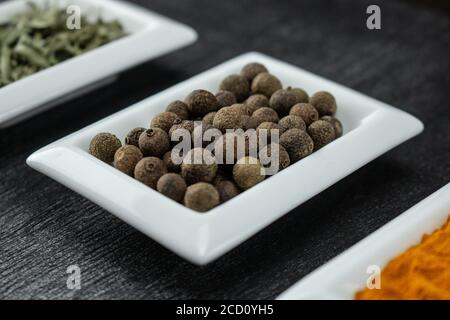 Allspice. Spezie colorate in ciotole bianche Condimenti per cucinare. Erbe e spezie naturali. Foto Stock