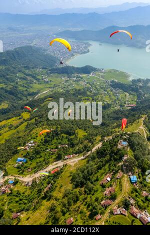 Vista aerea di un gruppo di parapendio volare sopra Sarangkot, giocando nelle terme, con la città di Pokhara e il lago Phewa in lontananza, su ... Foto Stock