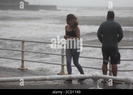 Aberystwyth Wales UK Weather 25 agosto 2020 : forti piogge e venti di Gale Force battter regioni costiere del Galles, forti venti guidare in enormi onde che sconfinano contro le difese marine di Aberystwyth. I vacanzieri coraggiosi venti di forza gale durante una passeggiata pomeridiana tempesta lungo la passeggiata, Credit: mike davies/Alamy Live News Foto Stock