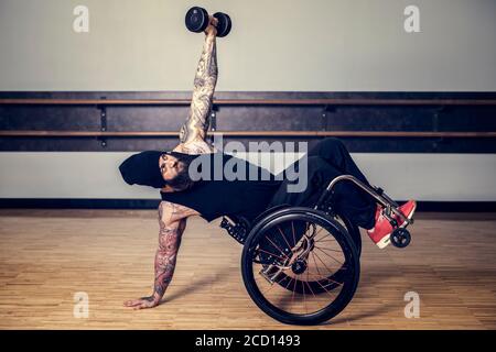 Un uomo paraplegico che schiocca una ruota nella sua sedia a rotelle ed equilibrando mentre solleva un peso in una palestra dopo... Foto Stock