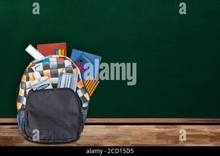 Concetto di educazione "back-to-School" nella nuova normale impostazione in classe che mostra lo zaino imbottito di cancelleria, igienizzatore per le mani e maschera facciale sul tavolo w Foto Stock