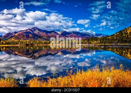 La catena montuosa si riflette sul lago Mentasta con foglie di colore autunnale sotto il cielo blu, Tok cutoff dalla Glenn Highway, Alaska centro-meridionale in autunno Foto Stock