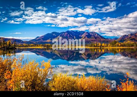 La catena montuosa si riflette sul lago Mentasta con foglie di colore autunnale sotto il cielo blu, Tok cutoff dalla Glenn Highway, Alaska centro-meridionale in autunno Foto Stock