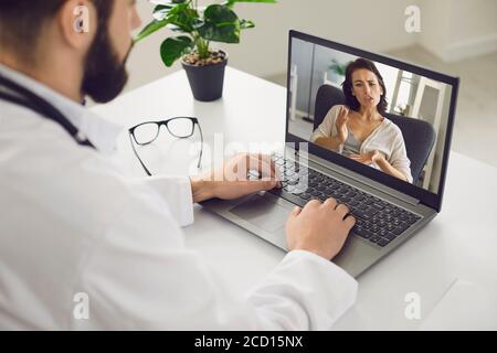 Consultazione medica online. Un uomo seduto nel suo ufficio usa un laptop, una videochiamata e ascolta un paziente. Foto Stock