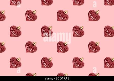 Motivo fatto di decorazioni rosse di Capodanno a forma di cuore su uno sfondo rosa pastello. Concetto creativo di festa. Foto Stock
