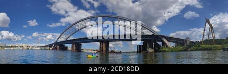 Costruzione di un nuovo ponte ad arco attraverso il fiume Dnieper, in primo piano un piccolo kayak con figure di persone, Kiev, Ucraina, panorama Foto Stock