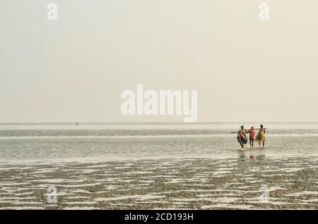 Pescatori che trasportano reti da pesca su pali oltre la spalla camminando sul mare a bassa marea; Chandipur, distretto di Baleswar, Stato di Odisha, India Foto Stock